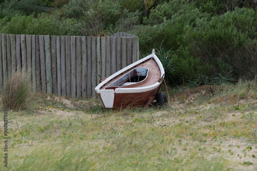 Lonely boat on sandy shore near fence and greenery in tranquil beach setting Lonely boat on sandy shore near fence and greenery in tranquil beach setting