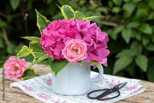 Blumenstrauß mit pink Rose und Hortensien-Blüten in rustikaler Emaille-Tasse	 photo