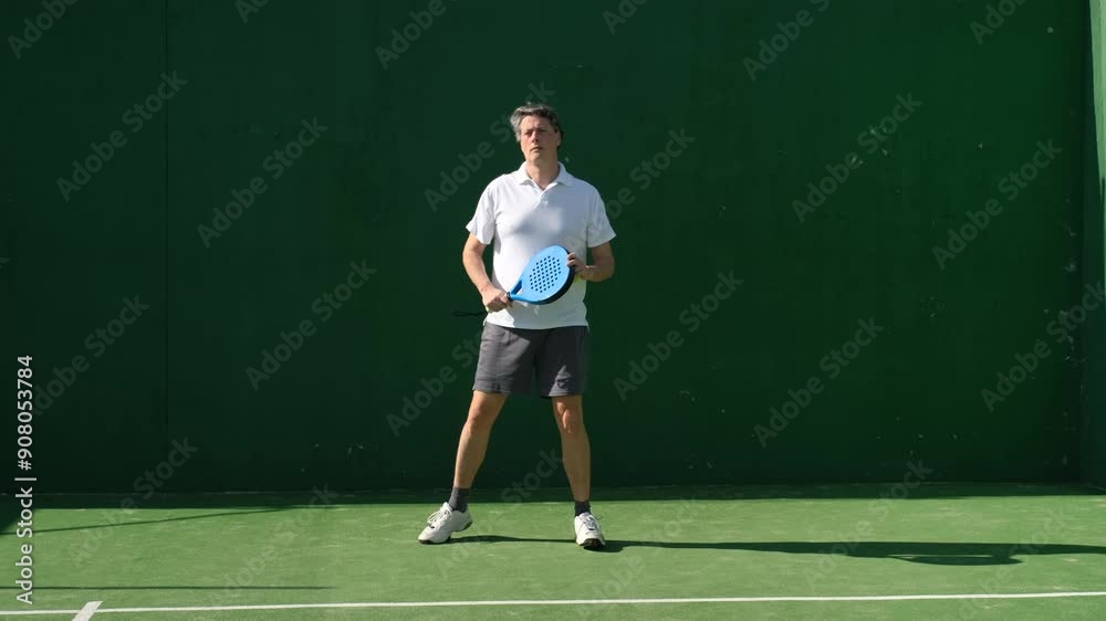 Man practicing paddle tennis outdoors, hitting ball against wall with focused movements under clear sunlight Man practicing paddle tennis outdoors, hitting ball against wall with focused movements under clear sunlight