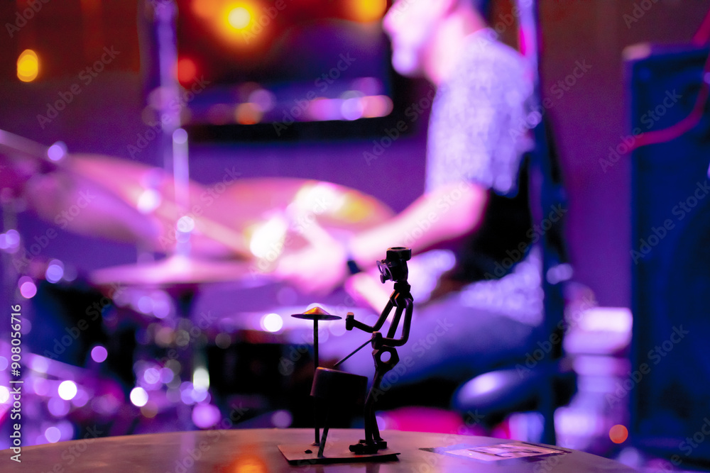 Silhouette of a miniature drummer sculpture with a live drummer playing in the background, creating a dynamic and artistic scene. Silhouette of a miniature drummer sculpture with a live drummer playing in the background, creating a dynamic and artistic scene.