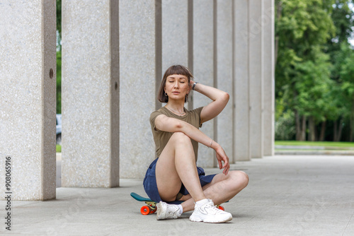 Картината върху платно Fashionable girl sits on a skateboard in a city park