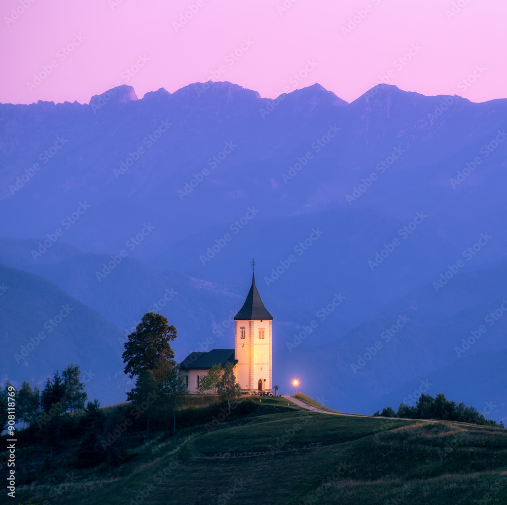 A church on a hill at sunset with mountain ranges in the background. Peaceful and serene atmosphere. Illuminated church against high alpine mountains and pink sky at twilight in Slovenia. Landscape A church on a hill at sunset with mountain ranges in the background. Peaceful and serene atmosphere. Illuminated church against high alpine mountains and pink sky at twilight in Slovenia. Landscape