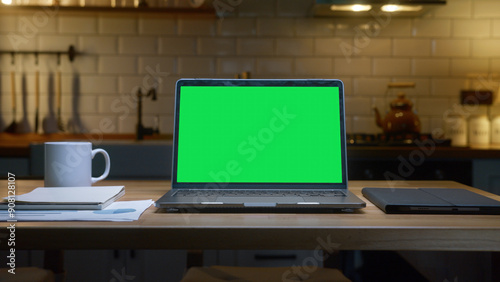 Fotografie A laptop with a green screen with a tablet, coffee cup and documents on a wooden table, emphasizing productivity and organization