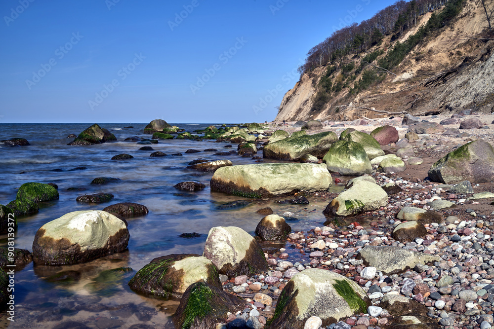 Baltic sea coast with boulders on the beach and cliff overgrown with trees on Wolin island Baltic sea coast with boulders on the beach and cliff overgrown with trees on Wolin island