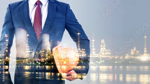 Double exposure of businessman or engineer hole orange helmet in hand with cooling tower of nuclear power plant oil and gas refinery plant background