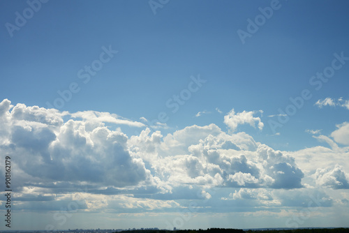 Whipped cream of cumulus clouds on a light blue sky. There is a light rain in the distance.