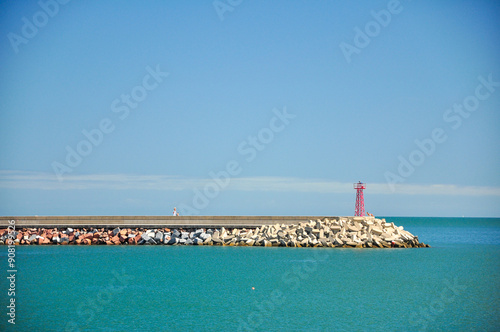 Breakwater with red beacon tower under clear blue sky in Piriapolis, Uruguay