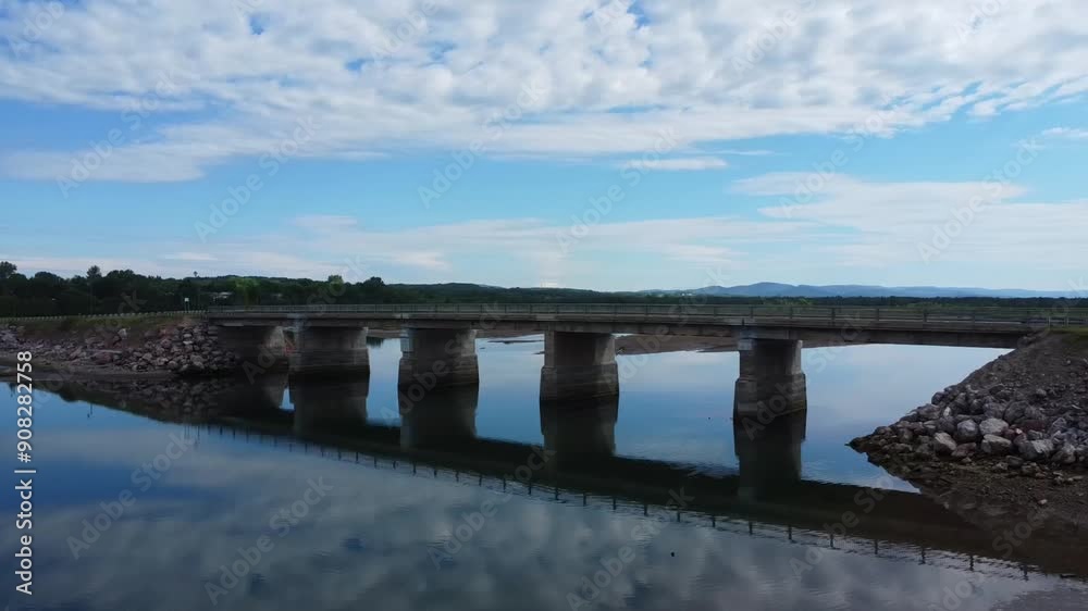Passage de drone sous le Pont Henri A. Leblanc, New-Richmond, Gaspésie, Québec. vers la Petite rivière Cascapédia. Les nuages et le bleu du ciel se reflêtant sur l'eau miroir de la Baie-des-Chaleurs.