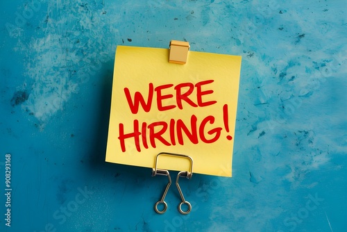 Blue background, yellow post it note with Were Hiring in red, metallic clip photo