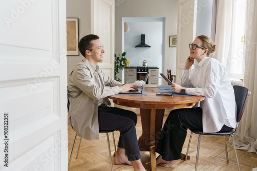 Wallpaper Mural Two people in casual attire working from home, sitting at a wooden table with laptops and tablets. Torontodigital.ca