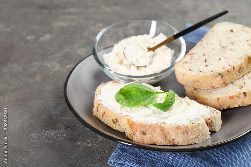 Pieces of bread with cream cheese and basil leaves on gray textured table, closeup. Space for text Pieces of bread with cream cheese and basil leaves on gray textured table, closeup. Space for text