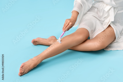 Woman shaving leg on light blue background, closeup