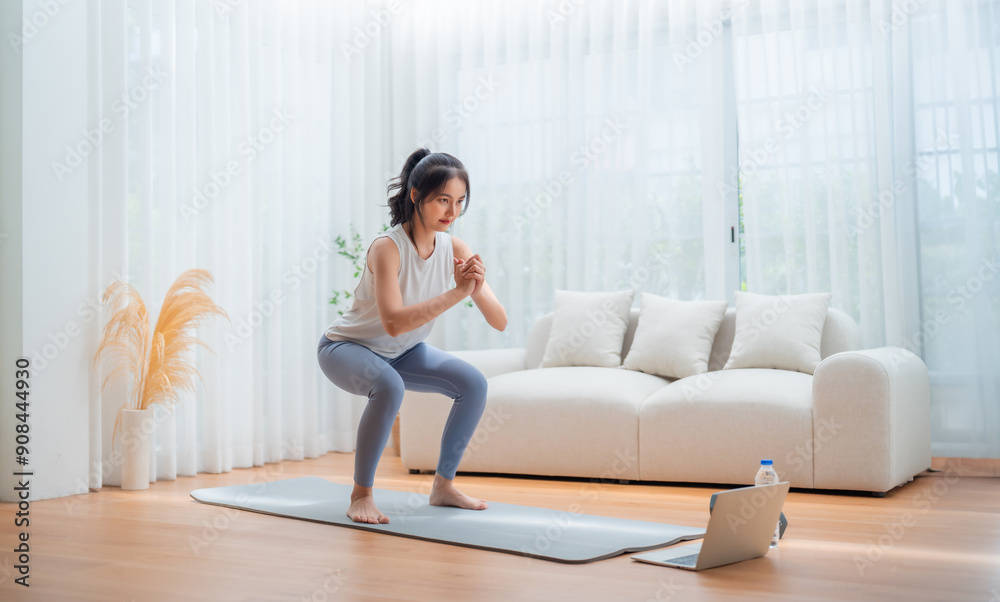 Young Asian beautiful woman doing aerobic exercise at home. Attractive girl doing workout by squatting, follow instructions video from online trainer for health in house Young Asian beautiful woman doing aerobic exercise at home. Attractive girl doing workout by squatting, follow instructions video from online trainer for health in house