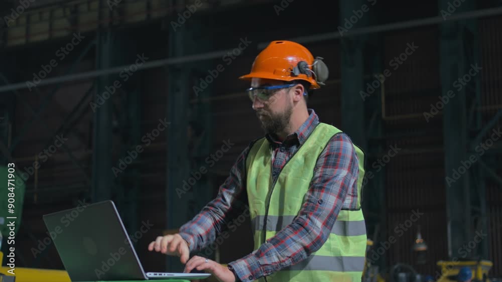 Professional heavy industry engineer in safety uniform and hard hat at manufacturing facility or factory. Male worker manages the work of industrial equipment and uses laptop computer. Slow motion. Professional heavy industry engineer in safety uniform and hard hat at manufacturing facility or factory. Male worker manages the work of industrial equipment and uses laptop computer. Slow motion.