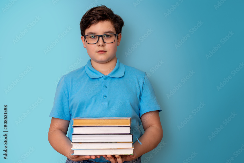 A serious boy, dark-haired, wearing glasses and a blue T-shirt, holding a stack of books A serious boy, dark-haired, wearing glasses and a blue T-shirt, holding a stack of books