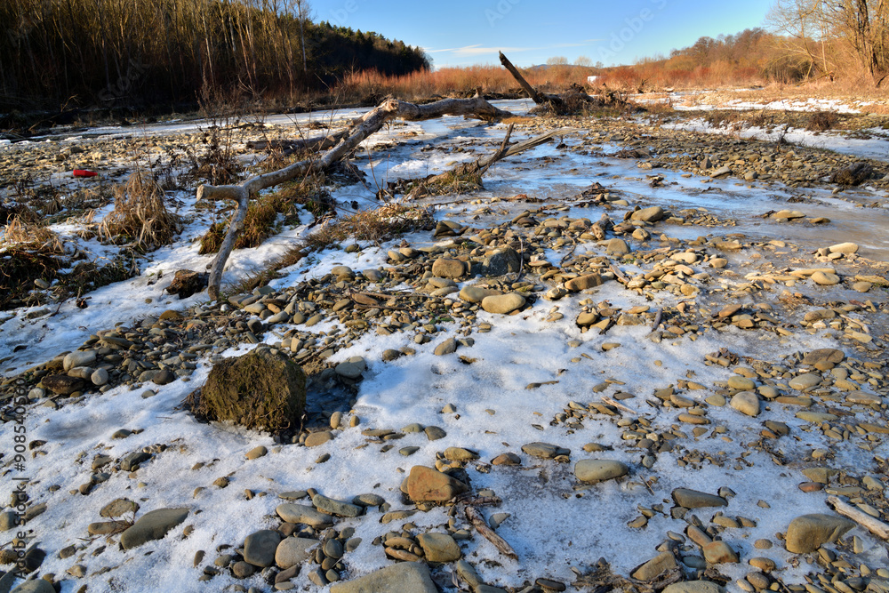 Obraz premium Eye view from below on a frozen river in winter flowing in the middle of the forest