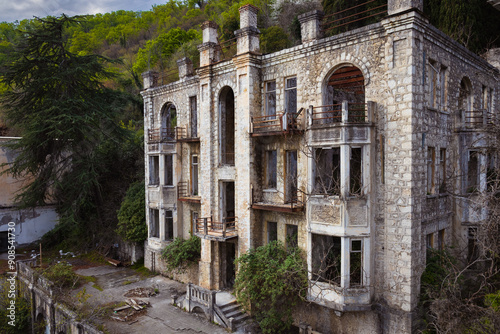 View of an abandoned ruined stone building overgrown with dense tropical tree at the foot of the mountain in old Gagra town in Abkhazia, Georgia
