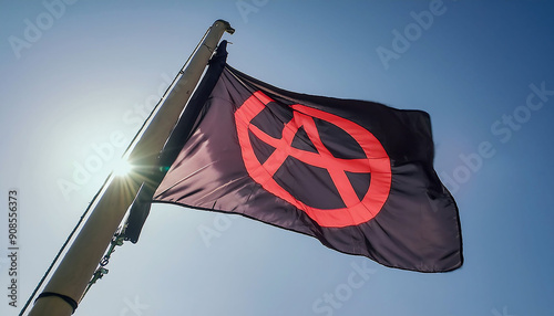 A black flag with the iconic red anarchist symbol stands out against a clear blue sky, capturing a message of rebellion and freedom. photo