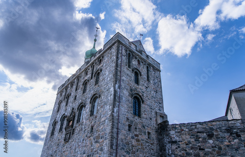 A stone pathway leads through a grand, arched gate towards the historic Bergenhus Fortress. The medieval-style tower and stone walls create a sense of antiquity. photo