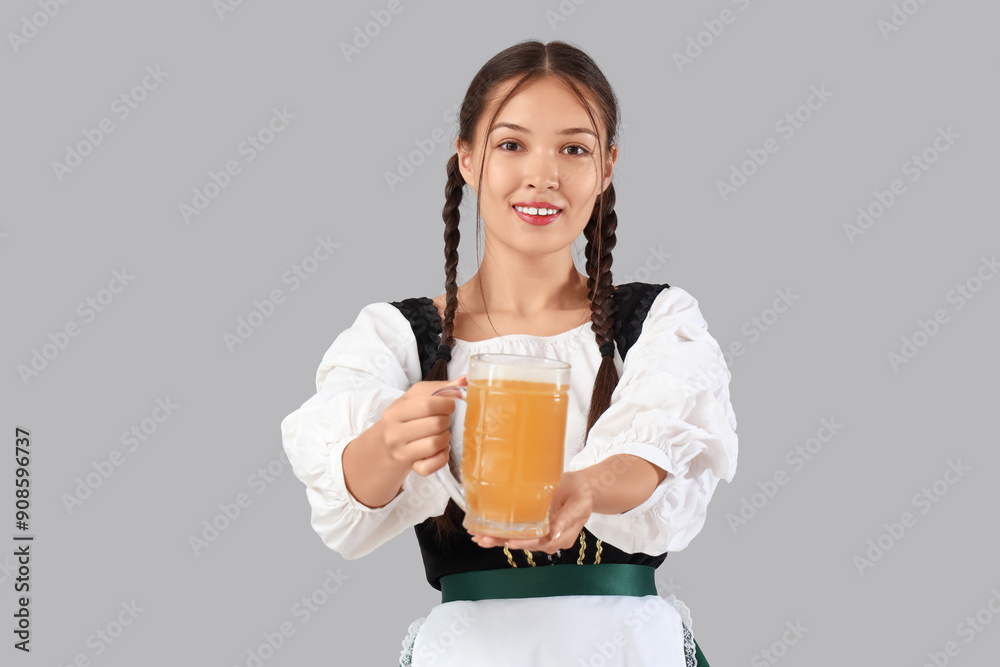 Beautiful young happy Asian Octoberfest waitress with mug of beer on grey background Beautiful young happy Asian Octoberfest waitress with mug of beer on grey background