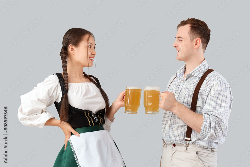 Young happy couple in traditional German clothes with mugs of beer on grey background Young happy couple in traditional German clothes with mugs of beer on grey background