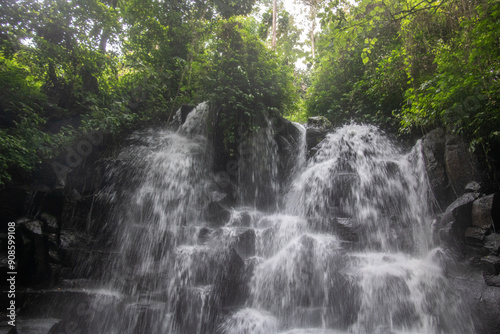 Fototapeta Naklejka Na Ścianę i Meble -  Beautiful hidden waterfall falling over multiple levels. surrounded by black lava stone Kanto Lampo, Bali, Indonesia