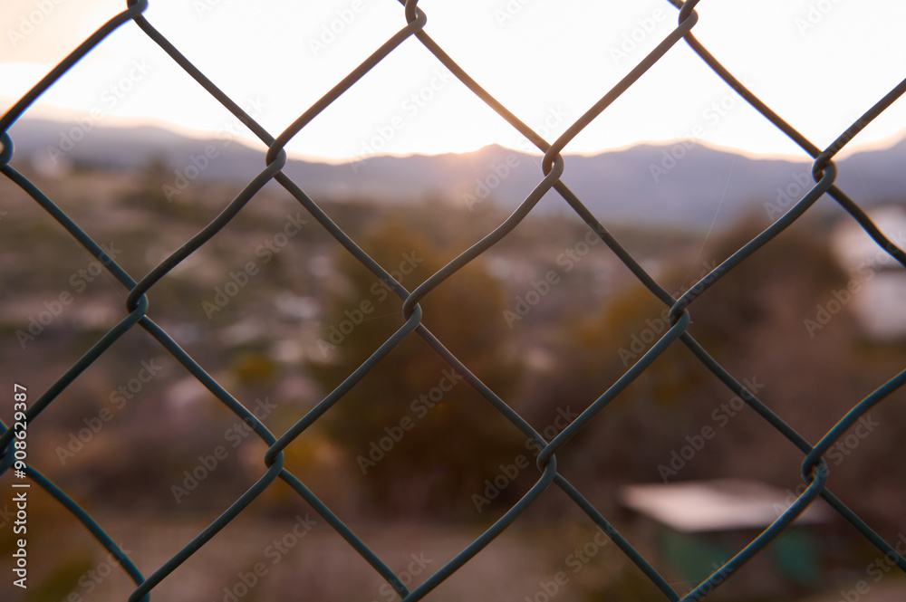 Chain link fence capturing blurred landscape during sunset Chain link fence capturing blurred landscape during sunset