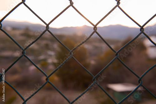 Chain link fence capturing blurred landscape during sunset