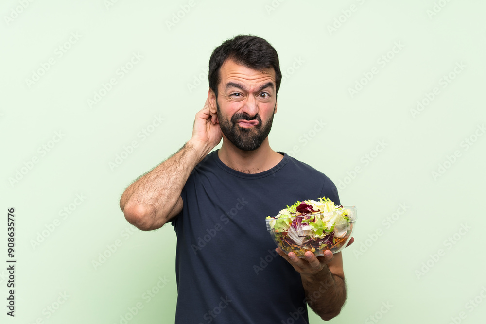 Young handsome man with salad over isolated green wall having doubts Young handsome man with salad over isolated green wall having doubts