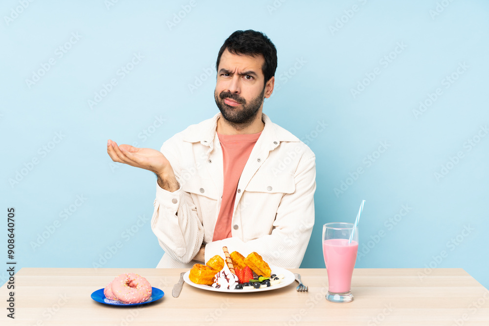 Man at a table having breakfast waffles and a milkshake unhappy for not understand something Man at a table having breakfast waffles and a milkshake unhappy for not understand something