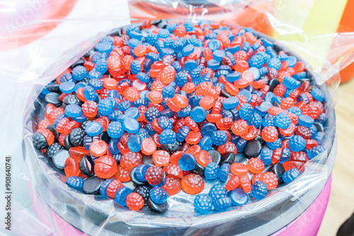 Close-up of large bowl filled with assorted gummy candies, surrounded by clear plastic wrap. The candies, in red, blue, and black, are displayed haphazardly, yet appealingly photo