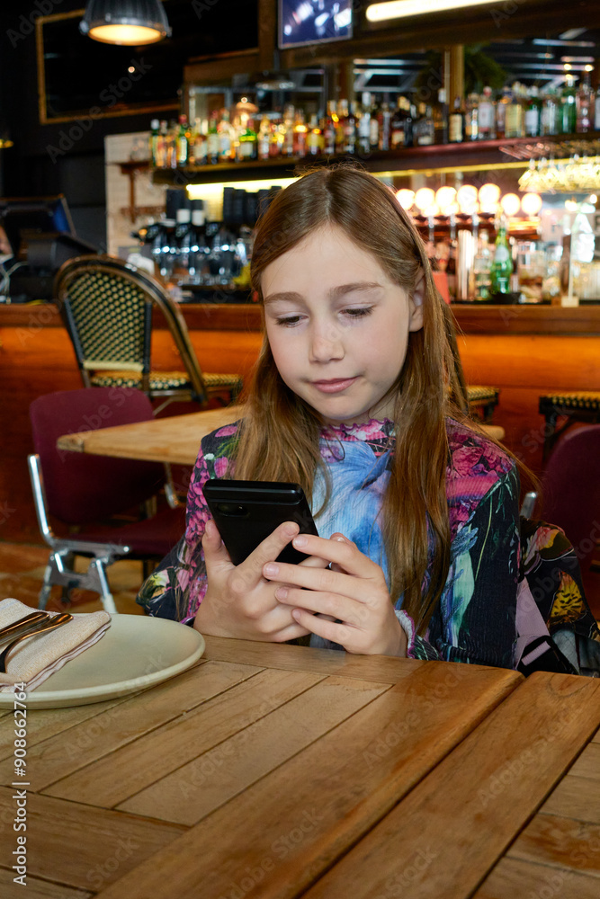 10 year old girl sitting in a restaurant reading on a smartphone while waiting for food, with a wooden table 10 year old girl sitting in a restaurant reading on a smartphone while waiting for food, with a wooden table