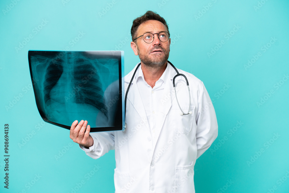 Middle age professional traumatologist doctor man isolated on blue background and looking up Middle age professional traumatologist doctor man isolated on blue background and looking up