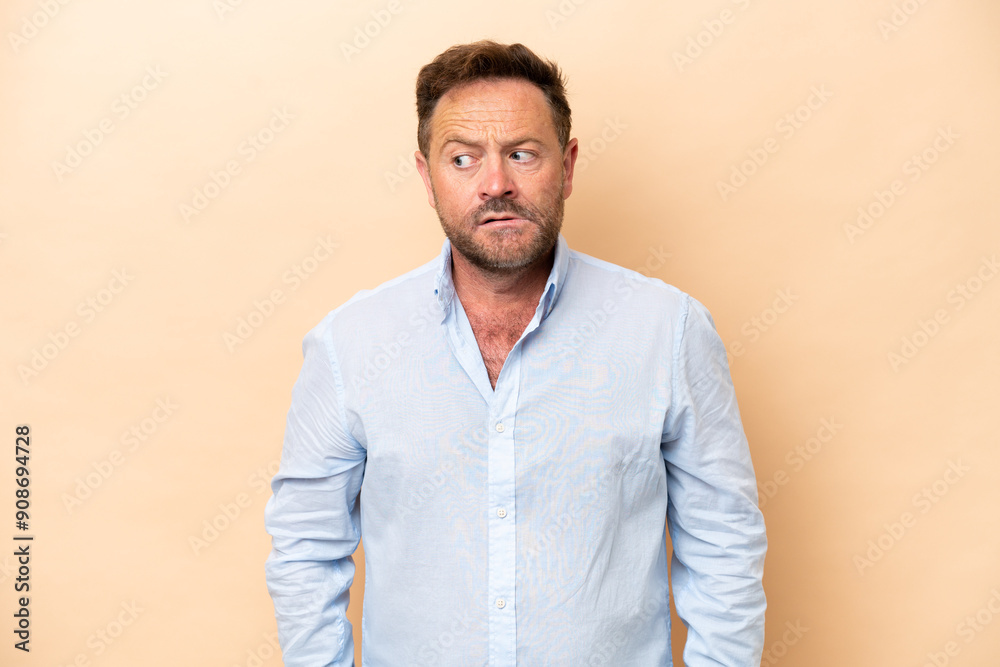 Middle age caucasian man isolated on beige background making doubts gesture looking side Middle age caucasian man isolated on beige background making doubts gesture looking side