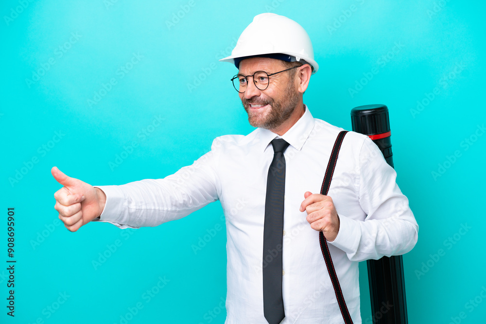 Middle age architect man with helmet and holding blueprints isolated on blue background giving a thumbs up gesture Middle age architect man with helmet and holding blueprints isolated on blue background giving a thumbs up gesture