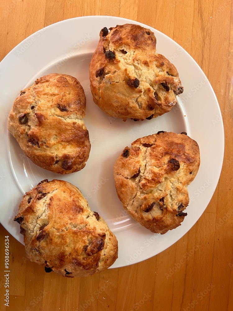 Fototapeta premium Scones shaped and cut in the shape of romantic heart fruit currant home made mix the four scones on grease proof paper baking tray for cooking flat lat view close up for valentine on white plate wood
