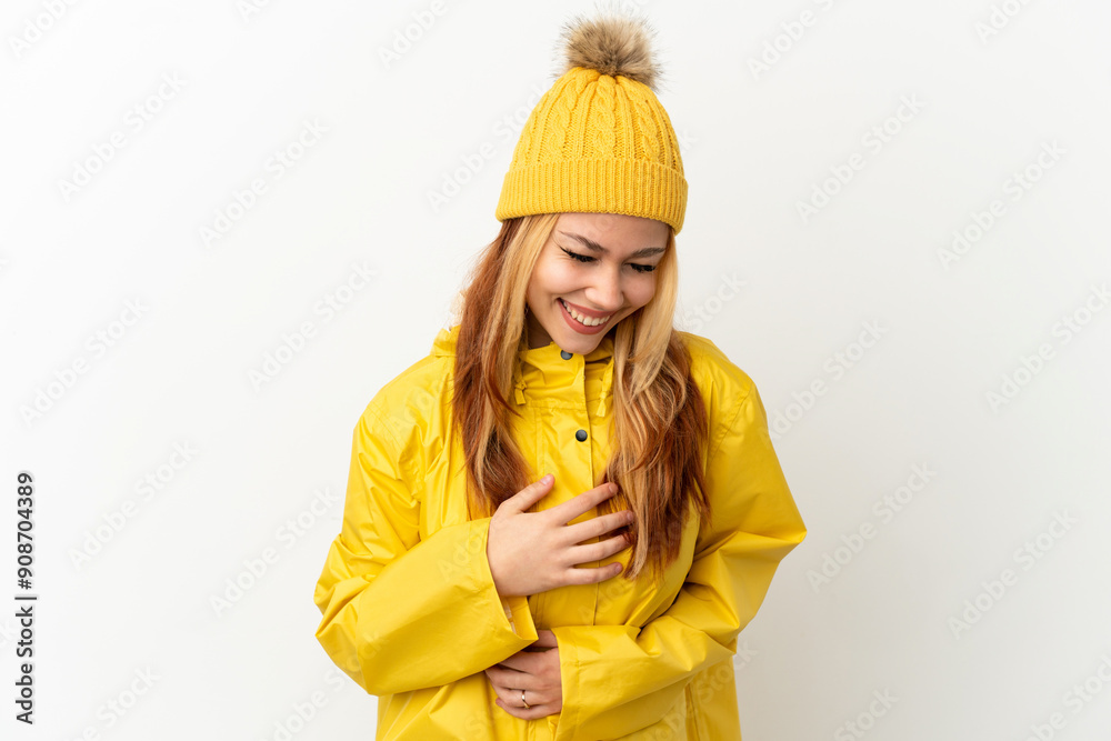 Teenager blonde girl wearing a rainproof coat over isolated white background smiling a lot Teenager blonde girl wearing a rainproof coat over isolated white background smiling a lot