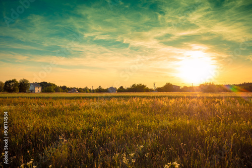 Rural landscape with beautiful gradient evening sky at sunset. Green field and village on the horizon