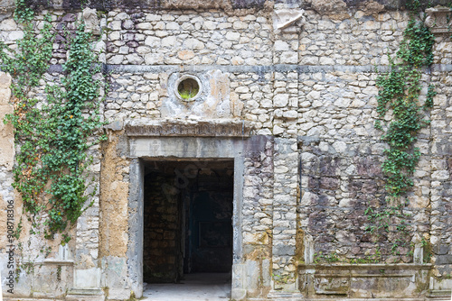 Empty doorway in the stone wall of a building. The stone wall of the house is covered with green ivy. Background with copy space