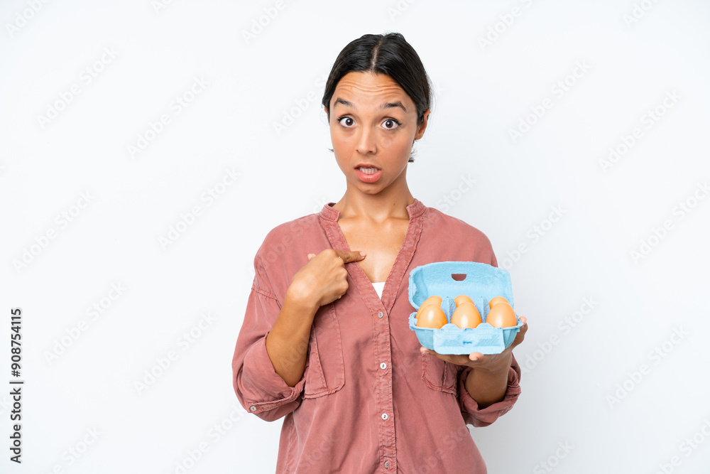Young hispanic woman holding eggs isolated on white background with surprise facial expression Young hispanic woman holding eggs isolated on white background with surprise facial expression