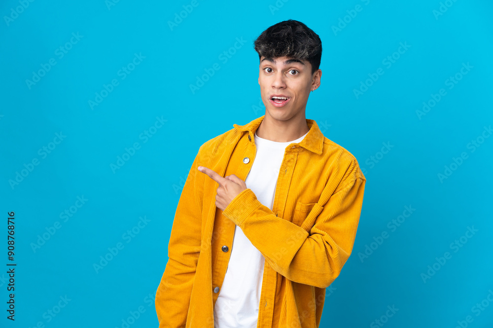 Young man over isolated blue background surprised and pointing side Young man over isolated blue background surprised and pointing side