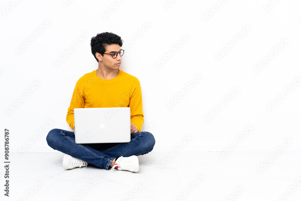 Venezuelan man sitting on the floor with laptop looking to the side Venezuelan man sitting on the floor with laptop looking to the side