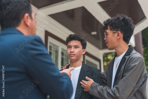A father trying to teach his son a lesson, criticizing his grades, while his brother tries to encourage him to do better. Showing tough love. Outdoor scene.