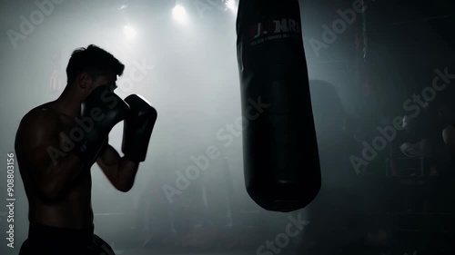 Professional african american boxer man punching bag in dynamic boxing action in ring of a sporting arena silhouette. Sportsman workout. Fitness box exercise. Active fit sport training indoor.