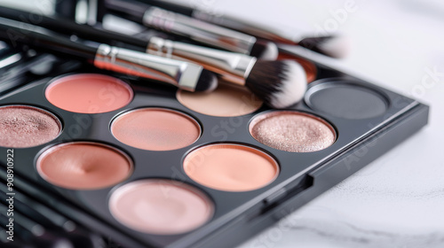 A sleek palette of makeup with brushes, showcasing a variety of nude and pink shades, resting on a white marble surface.