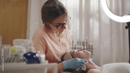 Skilled cosmetologist gently wiping the face of a relaxed female client during a facial treatment in a serene beauty salon setting.