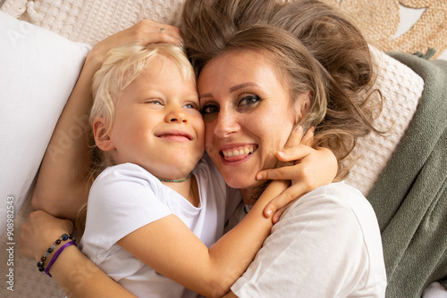 Portrait of happy mother and her little child son hugging on bed at home. Motherhood, affection