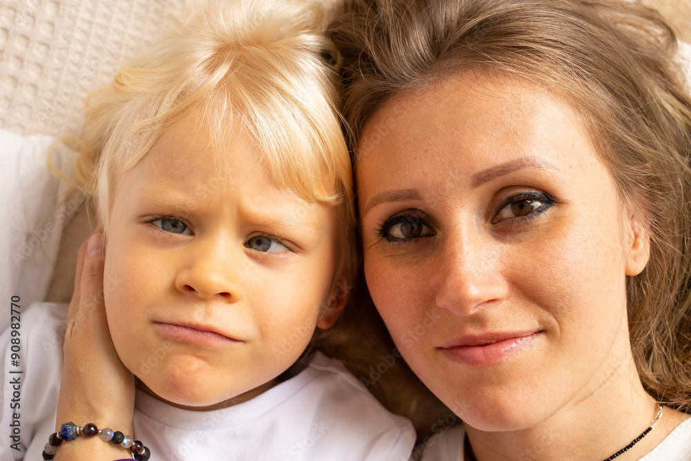 Portrait of mother and her little child baby boy hugging on bed at home. Child boy with strabismus eyes, squinting eyes, cross-eye. Motherhood, affection Portrait of mother and her little child baby boy hugging on bed at home. Child boy with strabismus eyes, squinting eyes, cross-eye. Motherhood, affection