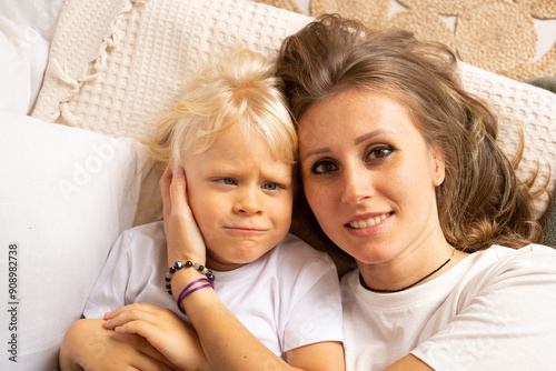 Portrait of mother and her little child boy son hugging on bed at home. Child boy with strabismus eyes, squinting eyes, cross-eye. Motherhood, affection