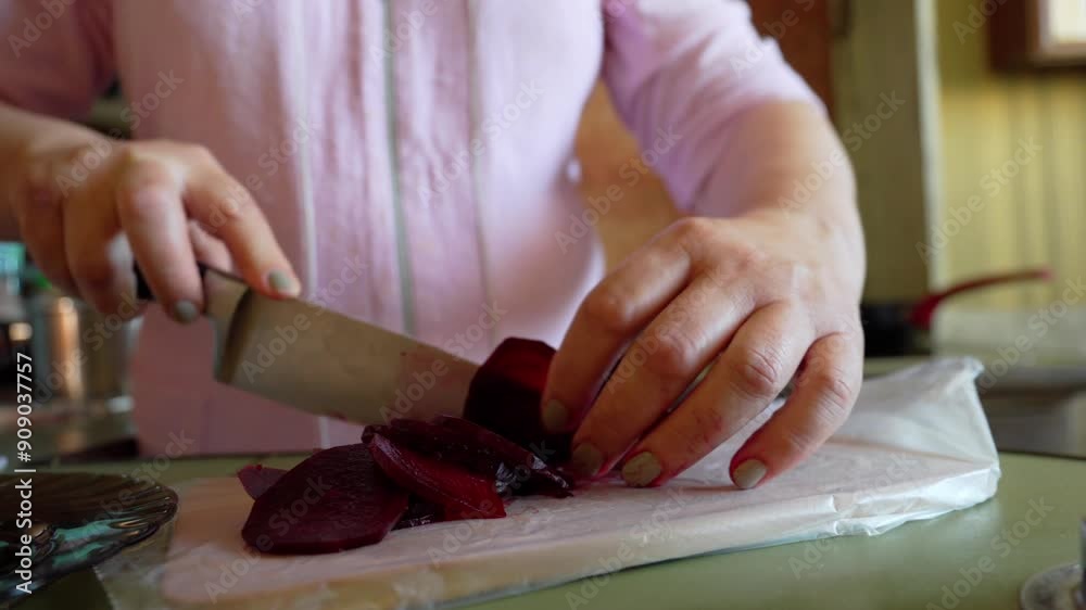 Holds a knife and slices a beetroot on a wooden board. The beetroot is wrapped in plastic wrap.